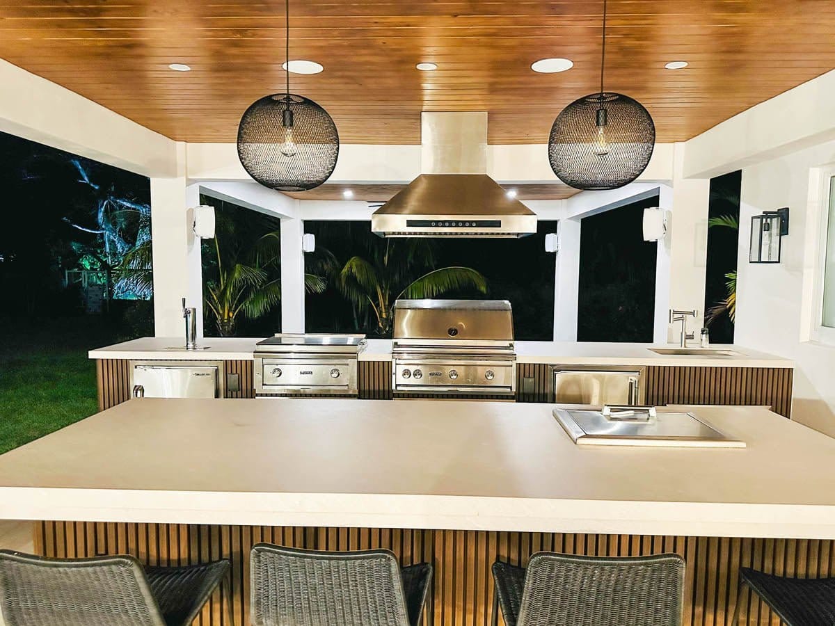 Modern outdoor kitchen with steel appliances, pendant lights, and Proline PLJI 102 Island Hood—1200 CFM. ProlineRangeHoods.com.