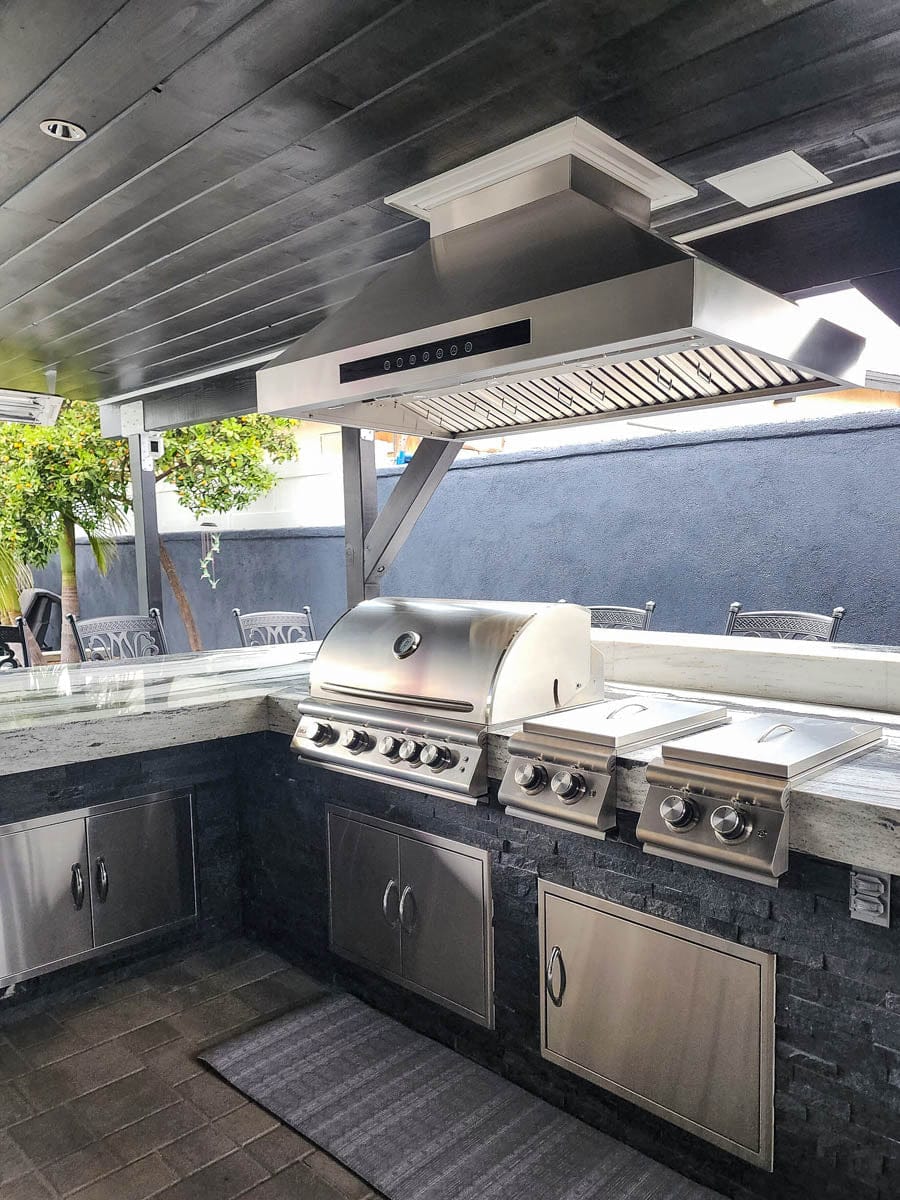Outdoor kitchen: grill, counter, bar seating, Proline PLJI 102 Range Hood—1200 CFM—under covered patio. ProlineRangeHoods.com.