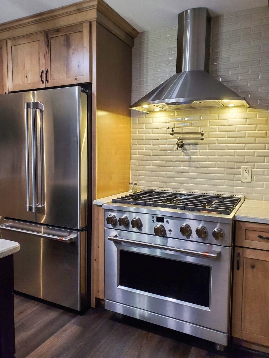 A modern kitchen featuring ProlineRangeHoods.com Vector hood with 600 CFM, set against white subway tile; fridge & oven.