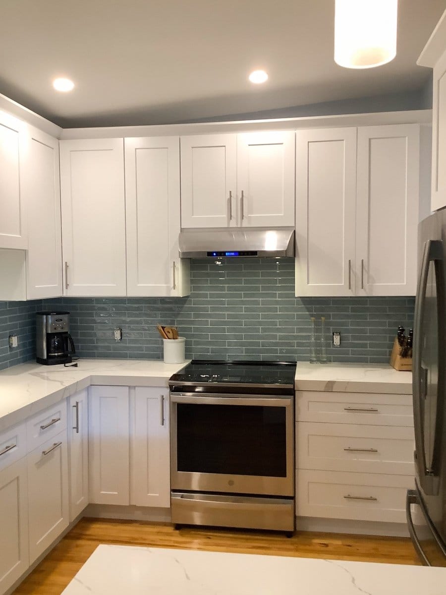 Modern kitchen with white cabinets, stainless steel appliances, and ProlineRangeHoods.com PLSW 117 under-cabinet range hood.