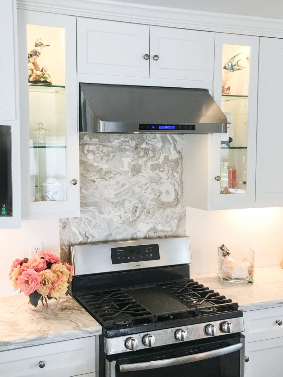 Modern kitchen with stainless steel stove, marble backsplash, white cabinets & ProlineRangeHoods.com PLJW 120 Range Hood.