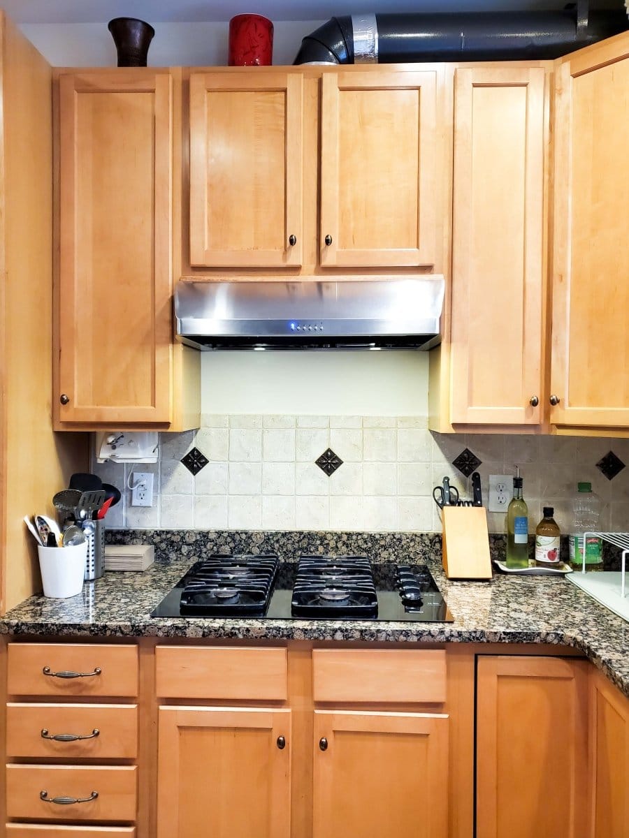 A kitchen with wooden cabinets has a ProlineRangeHoods.com sleek PLJW 125, 900 CFM stainless hood by the tiled backsplash.