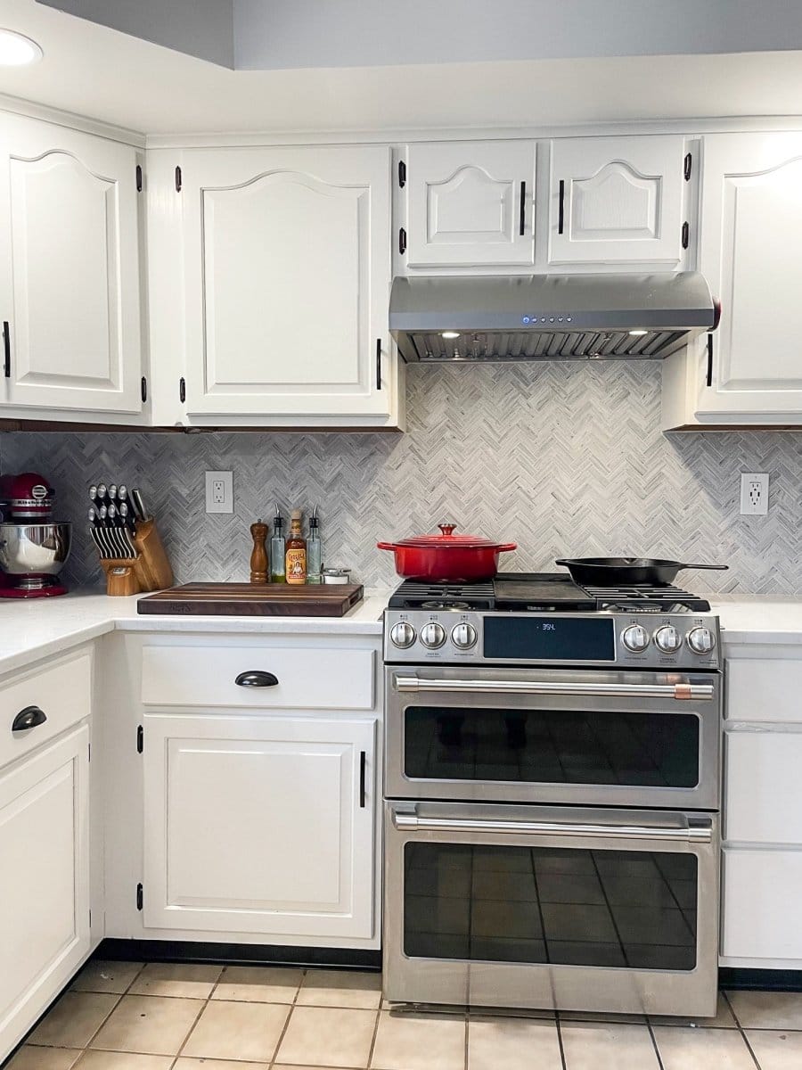 Modern kitchen: white cabinets, backsplash, red pot on stove, mixer. ProlineRangeHoods.com offers serene cooking with the Proline PLJW 125 stainless steel hood.
