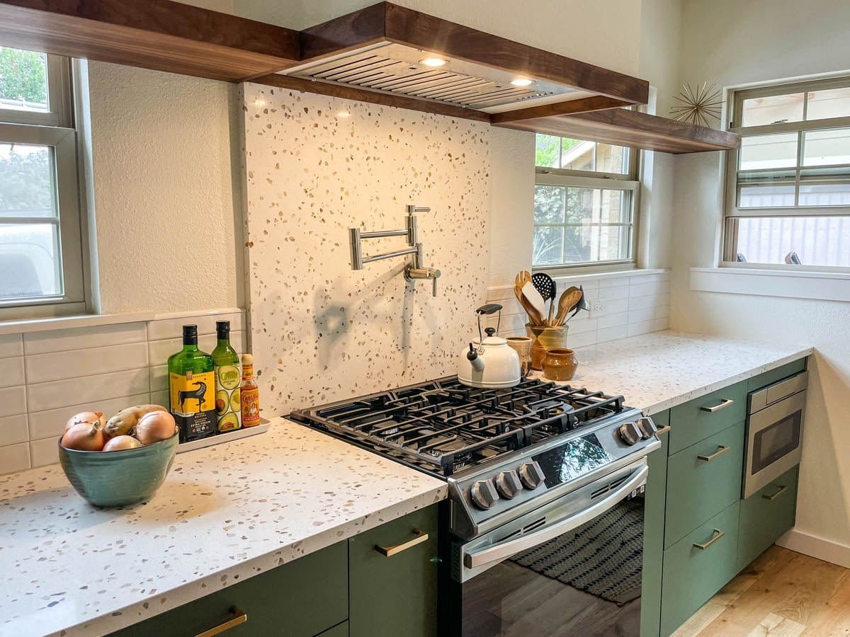 Modern kitchen with green cabinets, ProlineRangeHoods.com UMOD INS 600 CFM Hood, gas stove, speckled counters.