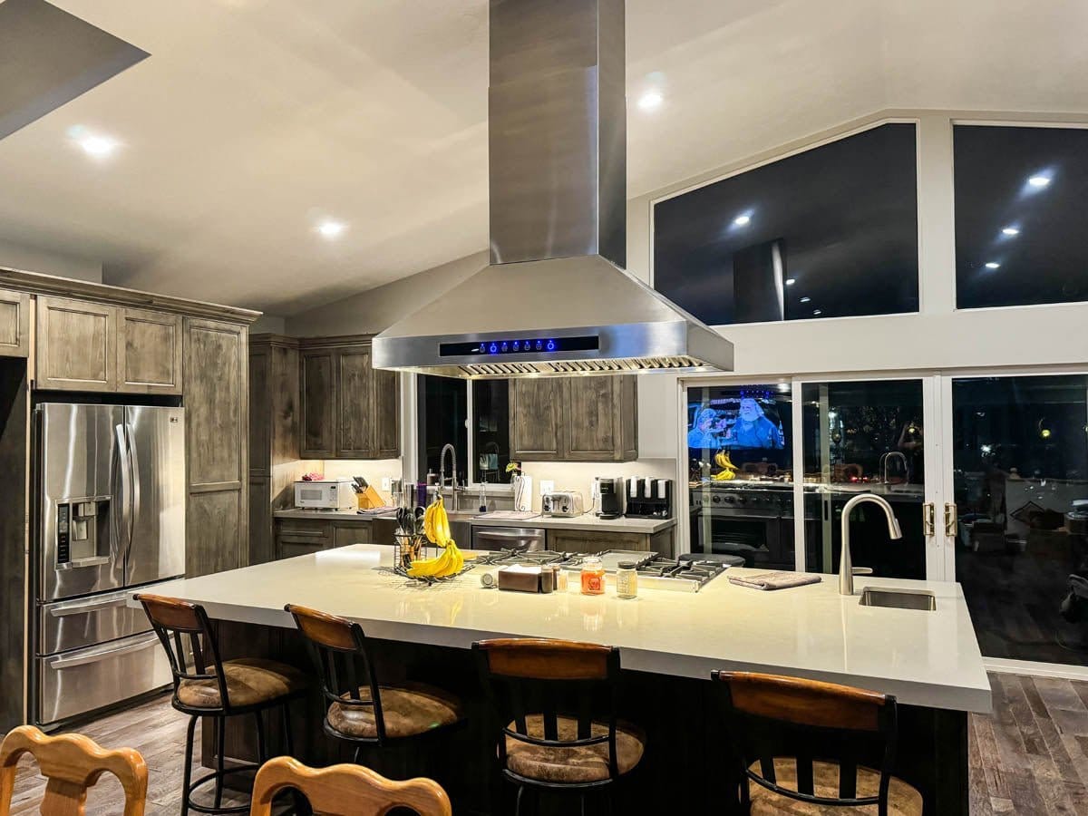 Modern kitchen with large island, bar stools, stainless steel appliances, Proline PLJI 102 hood; ProlineRangeHoods.com.