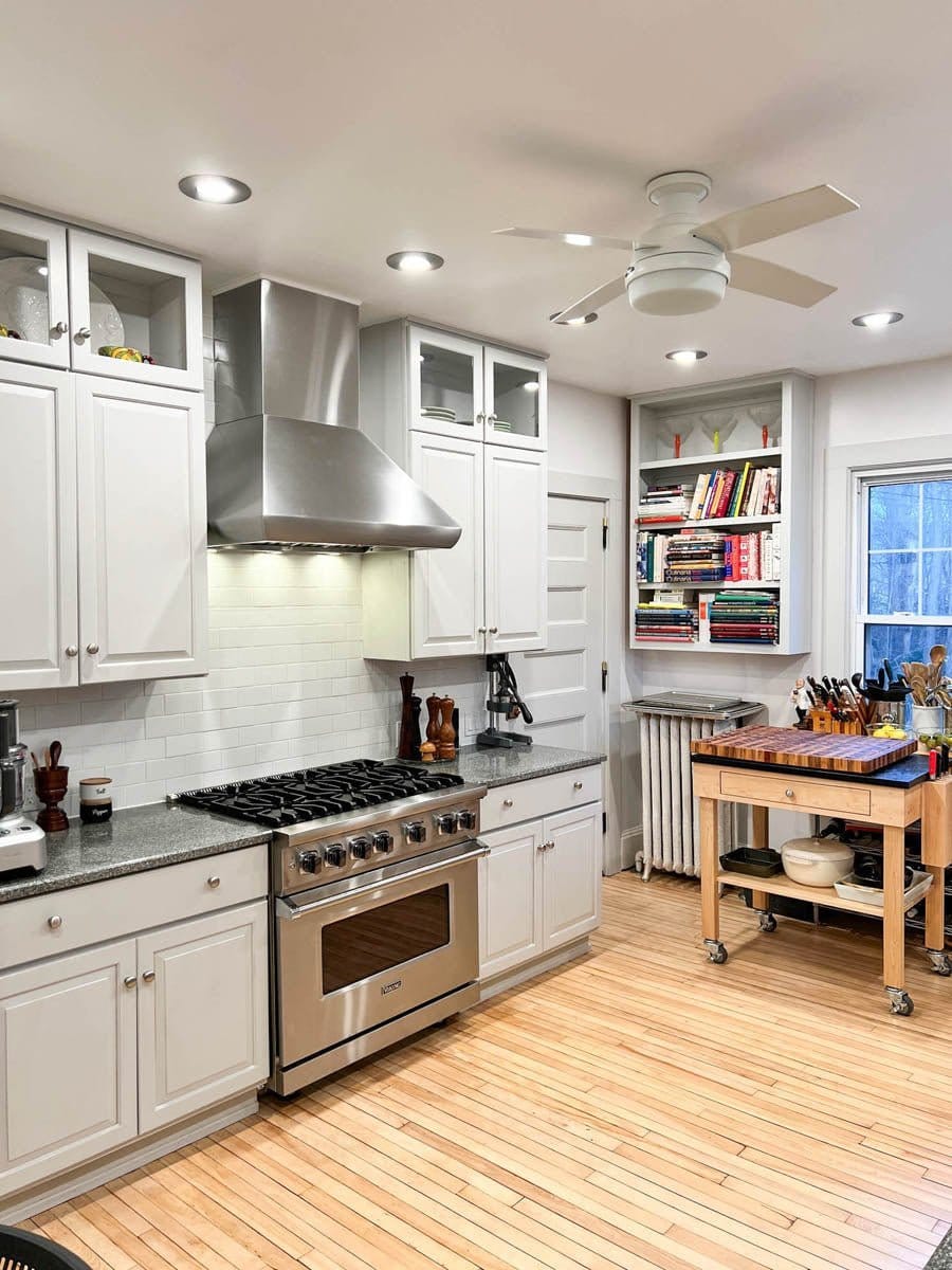 Modern kitchen with white cabinets, stainless stove, island, and Proline PLJW 109 WC hood—ProlineRangeHoods.com.