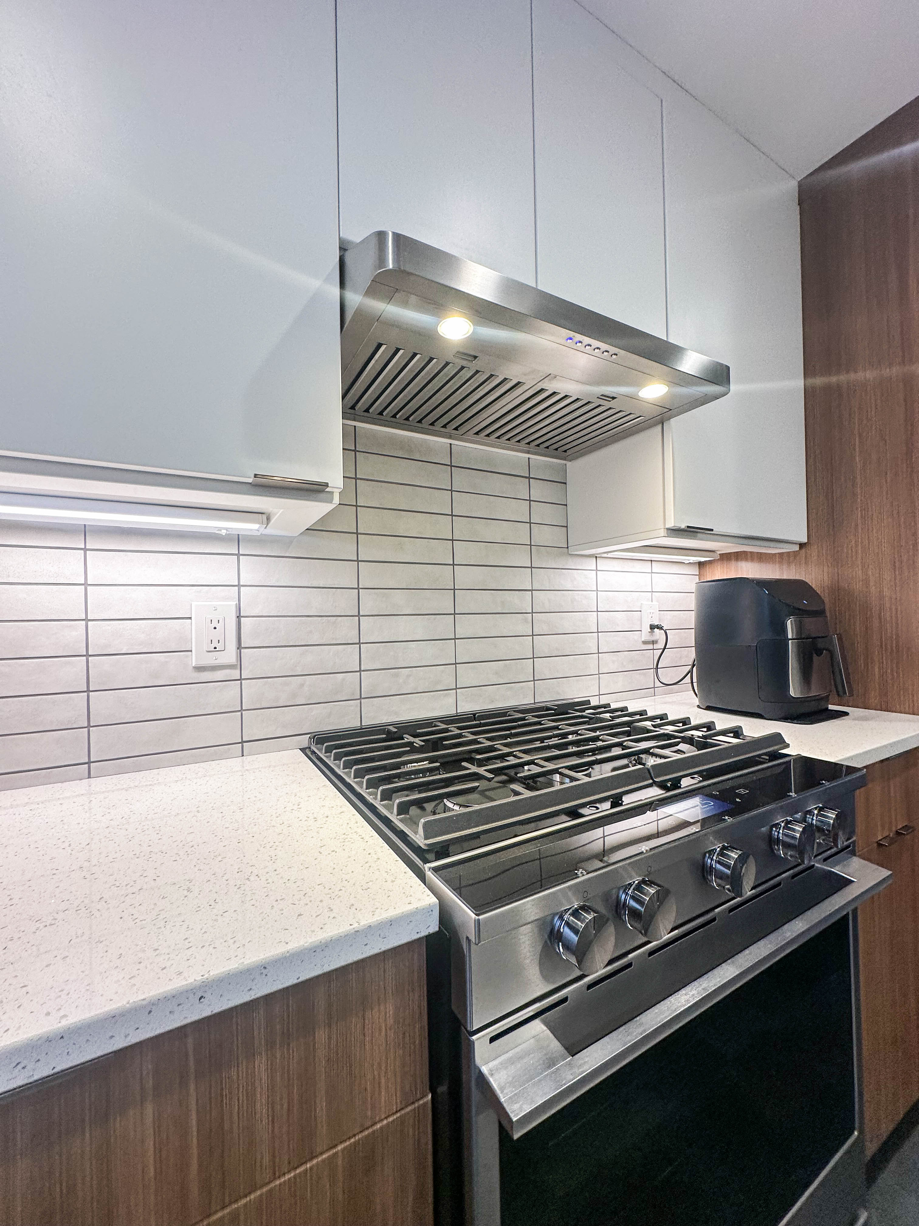 Modern kitchen with a 430 stainless stove, tiled backsplash, under-cabinet lighting, and ProlineRangeHoods.com PLJW 185 Slim.