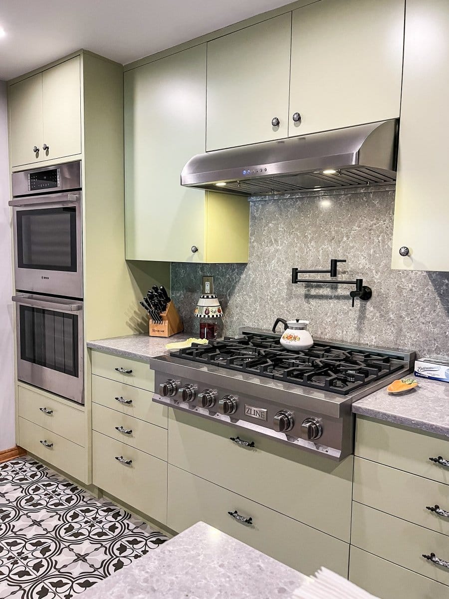 A modern kitchen with green cabinets features a ProlineRangeHoods.com hood in stainless steel, 900 CFM & ductless option.