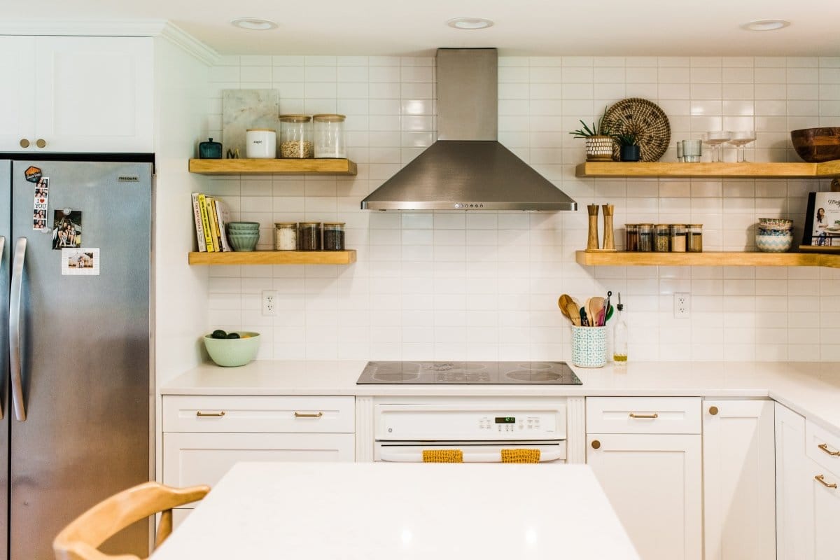 A contemporary kitchen with stainless steel appliances, wooden shelves, white cabinets, and a ProlineRangeHoods.com PLJW 129 range hood for superior ventilation.