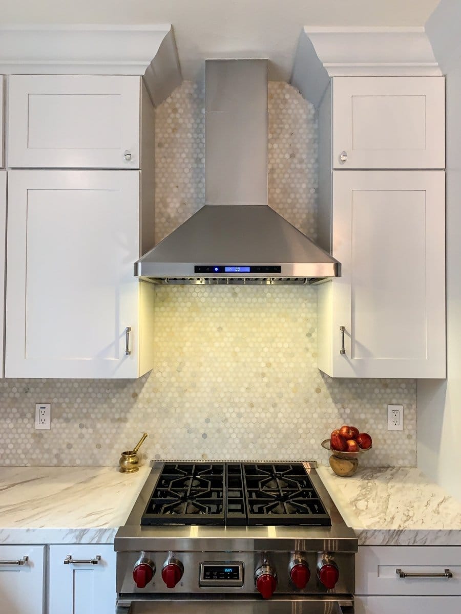 Modern kitchen with ProlineRangeHoods.com PLFW 129E, a sleek 900 CFM range hood, stainless stove, white cabinets, marble tops.