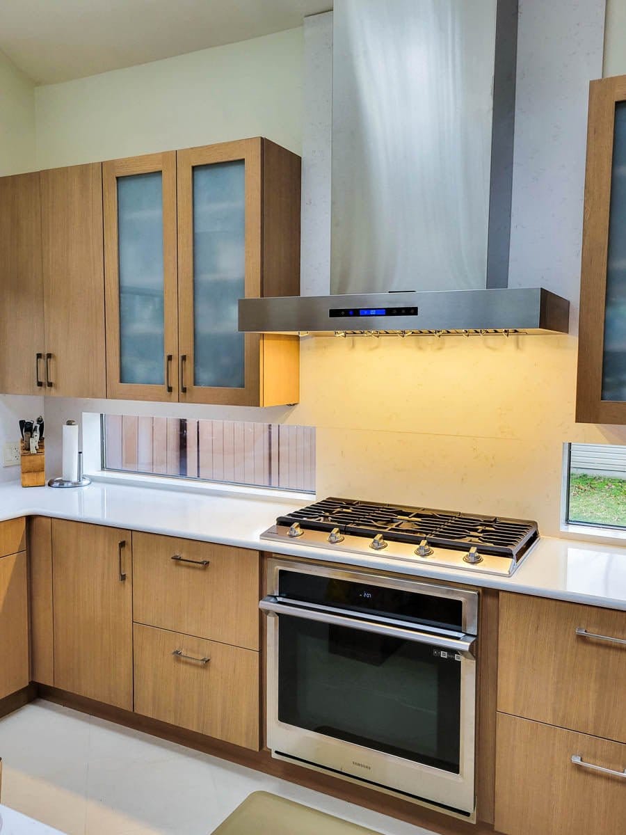 Modern kitchen with a stainless stove, oven, ProlineRangeHoods.com Wall Mounted Range Hood (1100 CFM), wood cabinets, white countertop.