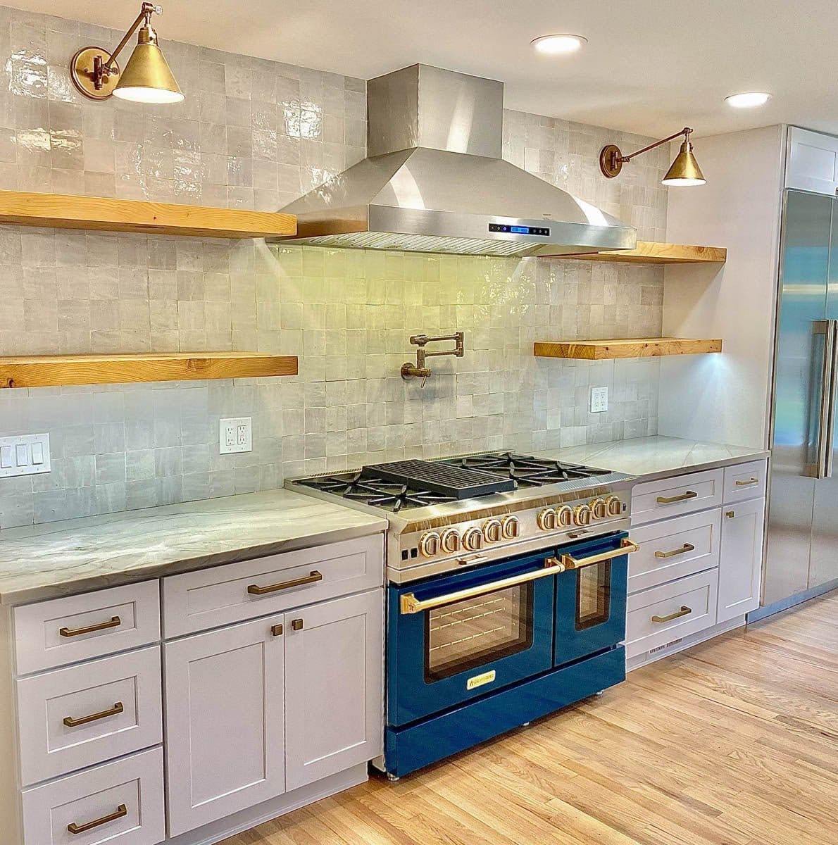 Modern kitchen with blue and gold range, Proline ProSW hood (ProlineRangeHoods.com), white cabinets, wood shelves, zellige tile.