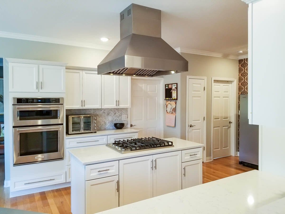 Modern kitchen with white cabinets, double oven, stovetop island, and a ProlineRangeHoods.com Island Hood in stainless steel.