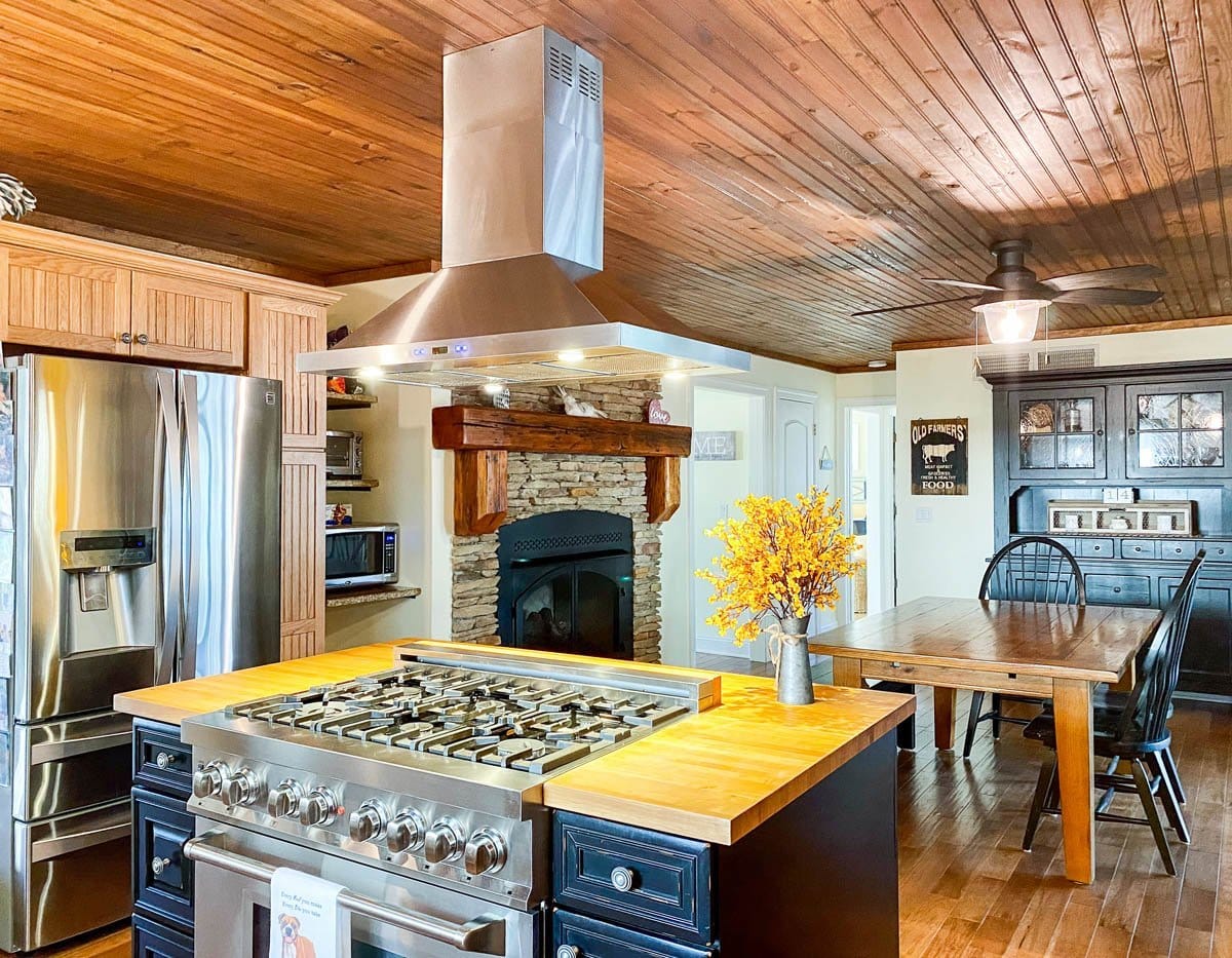 Bright rustic kitchen with stone fireplace, Proline PLFI 520 hood by ProlineRangeHoods.com, yellow flowers on table.