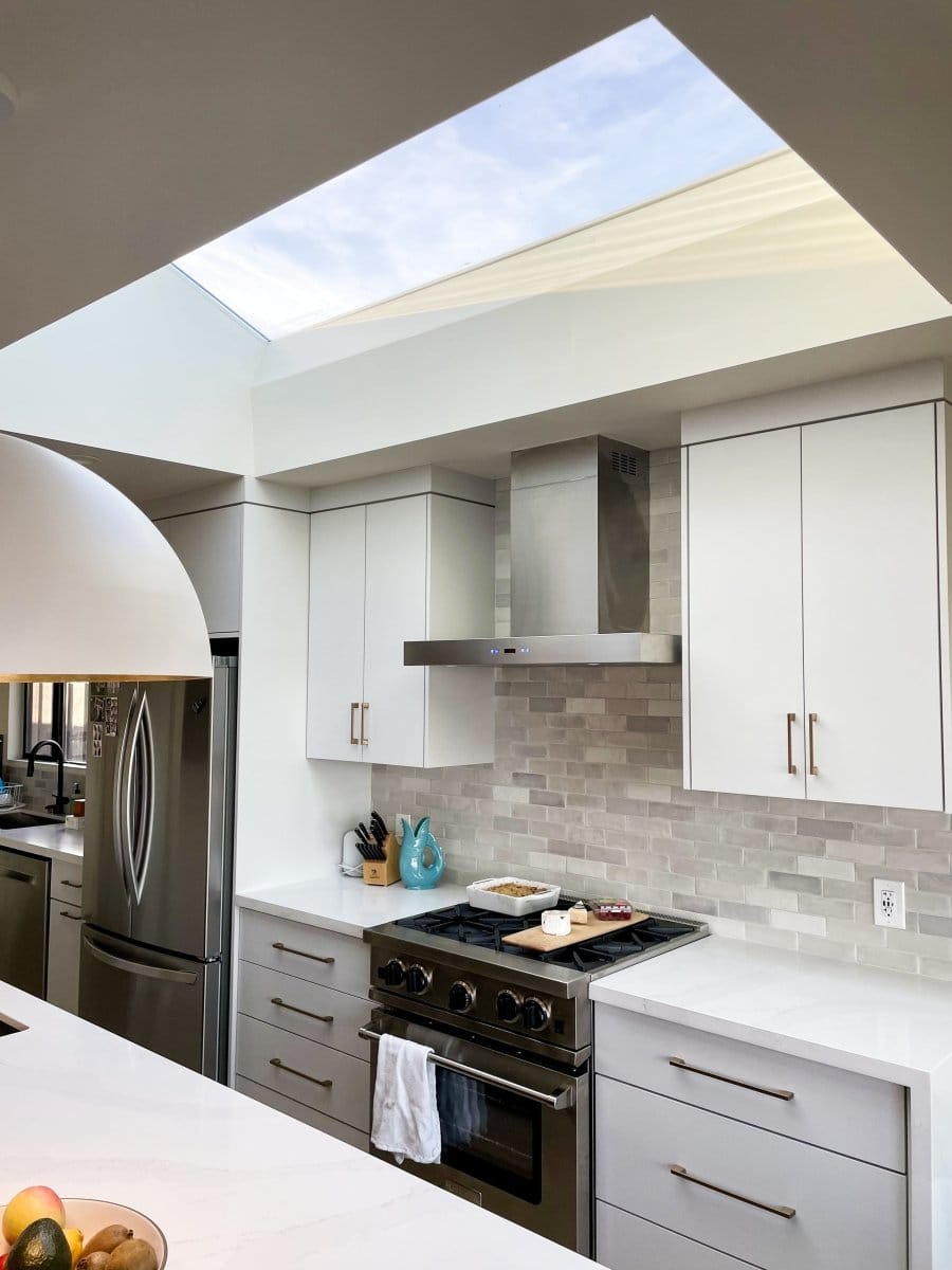 Contemporary kitchen with skylight, white cabinets, stainless steel appliances, marble countertops, and ProlineRangeHoods.com PLFW 750 wall-mounted range hood in sleek stainless steel finish for powerful airflow.