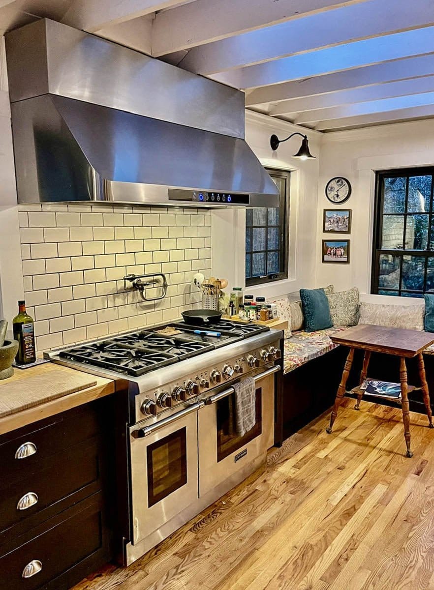 Modern kitchen with a PLJW 101 range hood from ProlineRangeHoods.com, white tiles, stainless stove, sunny breakfast nook.