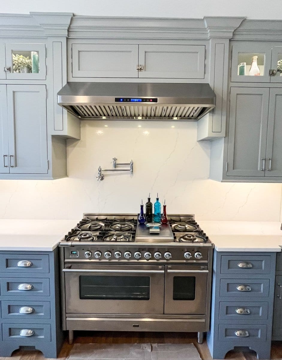 A modern kitchen at ProlineRangeHoods.com features their 900 CFM Under-Cabinet Hood in stainless steel, blue-grey cabinets, and elegant baffle filters.