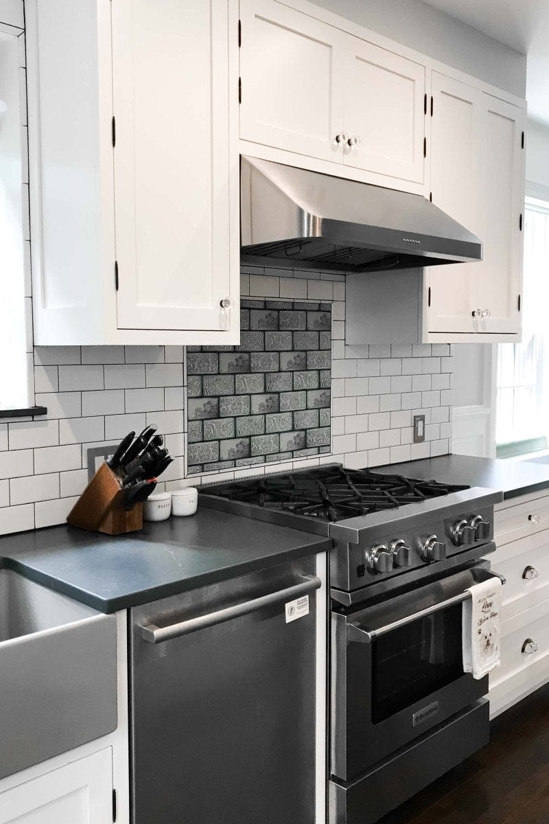 The kitchen boasts a modern design with ProlineRangeHoods.com white cabinets, stainless appliances, and a tiled backsplash.